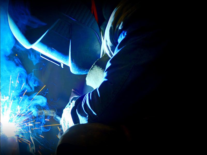Person wearing a welding mask with sparks and smoke.