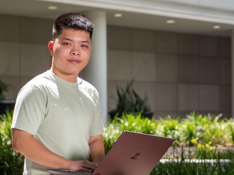 Student with a laptop sitting outdoors.